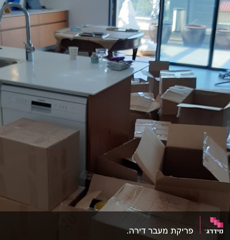 קופסאות קרטון פתוחות במטבח ליד אי לבן